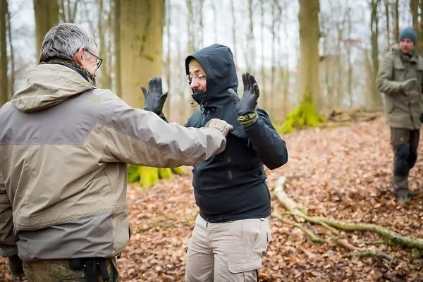 Zwei Personen üben eine Selbstverteidigungstechnik im Wald auf Laubboden