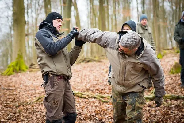 Zwei Personen üben eine Selbstverteidigungstechnik im Wald auf Laubboden