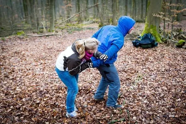 Zwei Personen üben eine Technik zur Selbstverteidigung im Laubwald