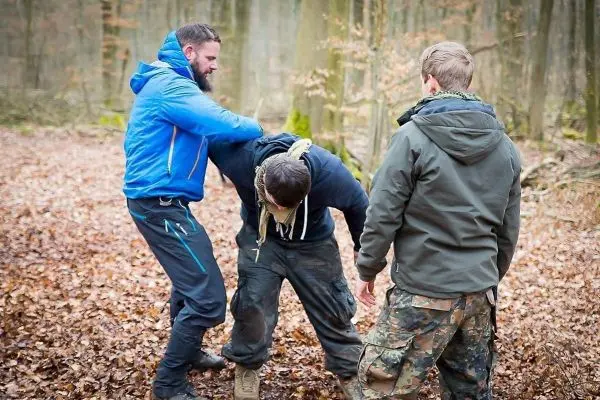Zwei Personen unterstützen einen dritten Mann in einer Waldumgebung