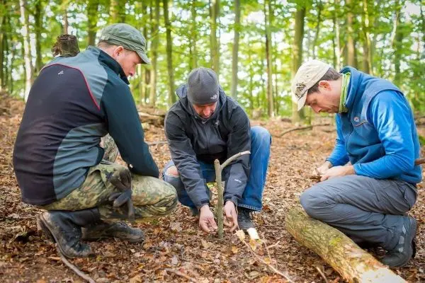 Drei Personen arbeiten gemeinsam an einer selbstgebauten Schlagfalle im Wald
