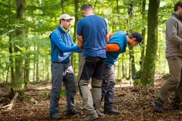 Drei Personen helfen einem Mann, der mit Handschellen gefesselt ist, im Wald