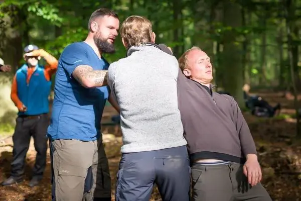 Drei Personen üben eine Technik zur Unterstützung in einer Notsituation im Wald