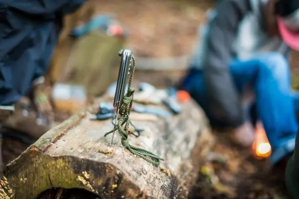 Ein Messer steht auf einem Baumstamm mit Ausrüstung im Hintergrund