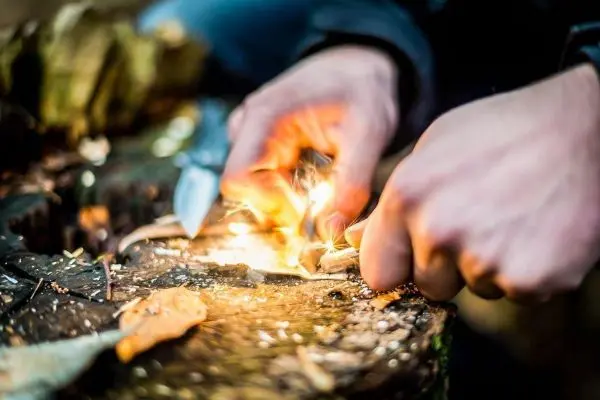 Feuerstahl erzeugt Funken auf Zunderstück auf einem Baumstamm