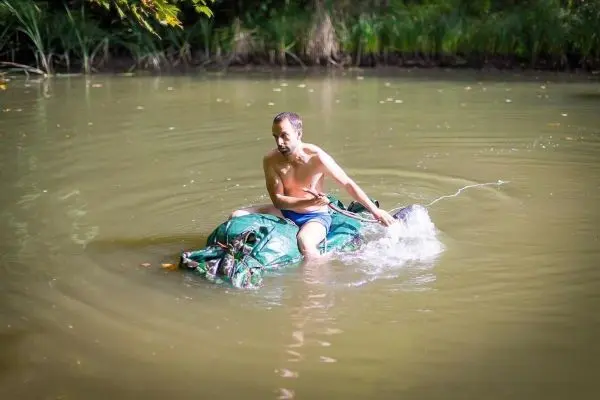 Junge sitzt auf improvisiertem Floß und paddelt im Wasser