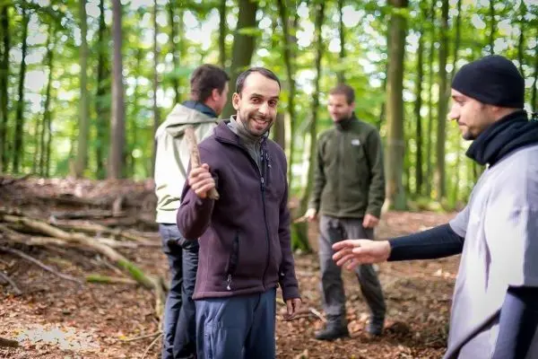 Mann hält einen Stock in der Hand, umgeben von anderen Personen im Wald
