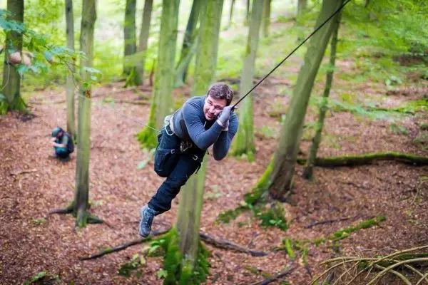 Mann hängt an einem Seil zwischen Bäumen in einem Wald