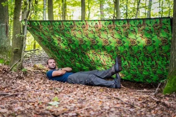 Mann liegt unter einer Tarp-Notunterkunft im Wald auf dem Boden