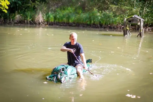 Mann paddelt auf einem improvisierten Floß durch einen ruhigen Gewässerabschnitt