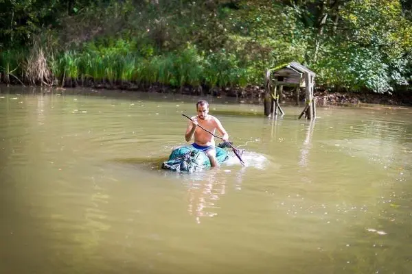 Mann paddelt auf improvisiertem Floß mit einem Stock durch einen See