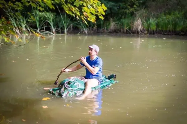 Mann paddelt mit einem Stock auf einem improvisierten Floß im Wasser