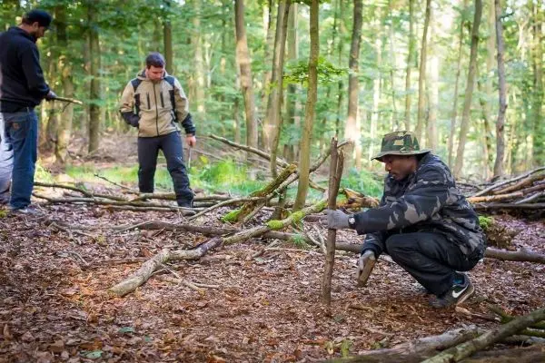 Mann positioniert einen Stock für eine selbstgebaute Schlagfalle im Wald