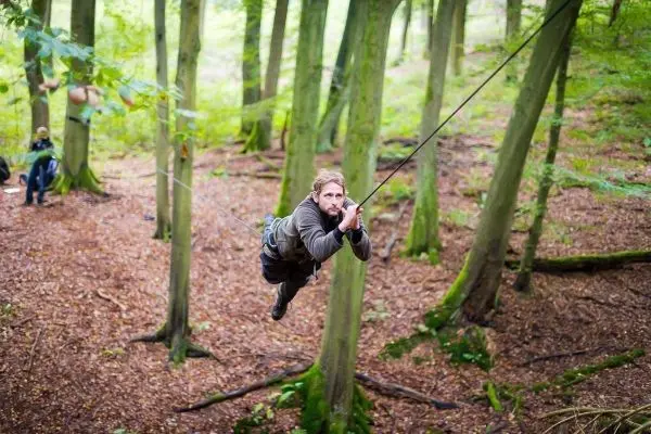 Mann überquert eine selbstgebaute Seilbrücke zwischen Bäumen