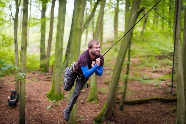 Mann überquert eine selbstgebaute Seilbrücke zwischen Bäumen