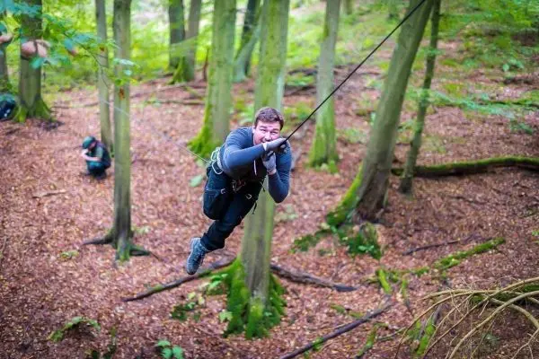 Mann überquert eine selbstgebaute Seilbrücke zwischen Bäumen