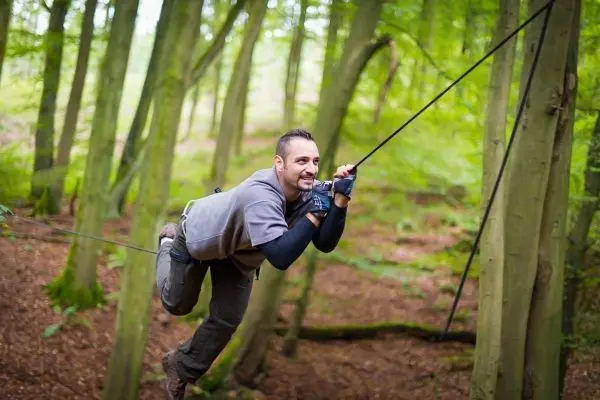 Mann überquert eine selbstgebaute Seilbrücke zwischen Bäumen