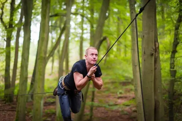 Mann überquert eine selbstgebaute Seilbrücke zwischen Bäumen