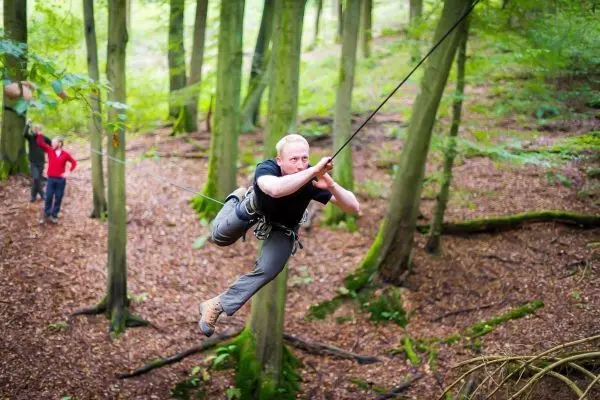 Mann überquert eine selbstgebaute Seilbrücke zwischen Bäumen im Wald