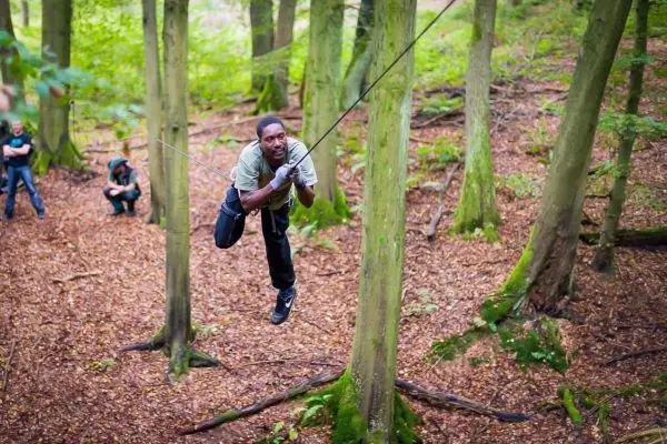 Mann überquert eine selbstgebaute Seilbrücke zwischen Bäumen im Wald
