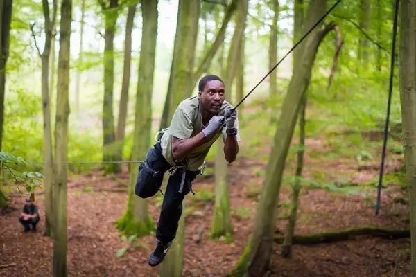 Mann überquert selbstgebaute Seilbrücke zwischen Bäumen im Wald