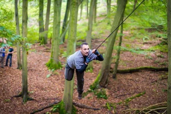 Mann überquert selbstgebaute Seilbrücke zwischen Bäumen im Wald