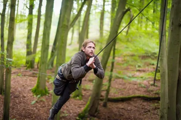 Mann überquert selbstgebaute Seilbrücke zwischen Bäumen im Wald