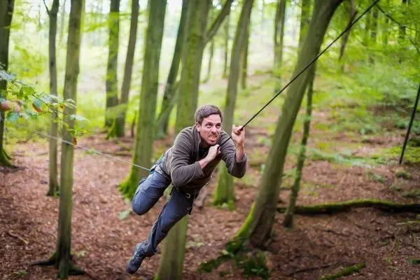 Mann überquert selbstgebaute Seilbrücke zwischen Bäumen im Wald
