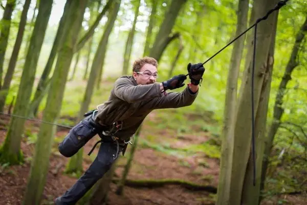 Mann überquert selbstgebaute Seilbrücke zwischen Bäumen im Wald