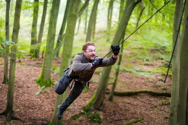 Mann überquert selbstgebaute Seilbrücke zwischen Bäumen im Wald