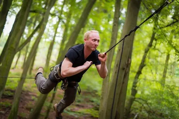 Mann überquert selbstgebaute Seilbrücke zwischen Bäumen im Wald
