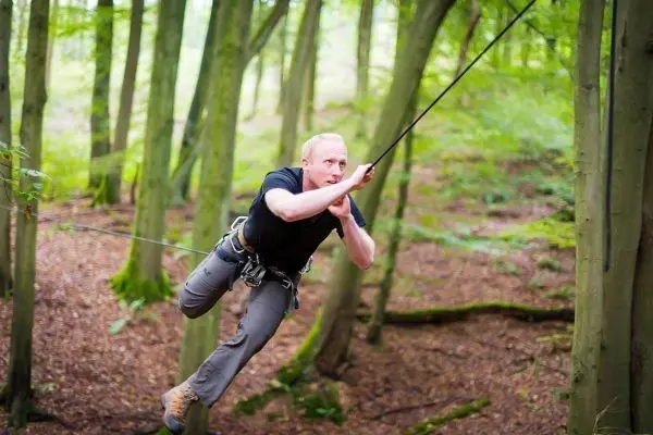 Mann überquert selbstgebaute Seilbrücke zwischen Bäumen im Wald