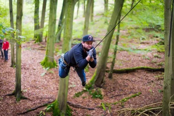 Mann überquert selbstgebaute Seilbrücke zwischen Bäumen im Wald