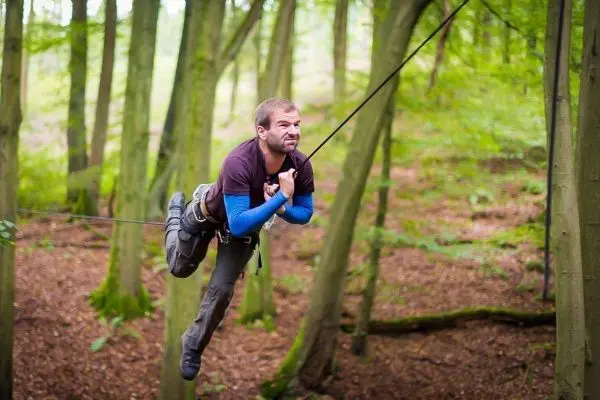 Mann überquert selbstgebaute Seilbrücke zwischen Bäumen im Wald