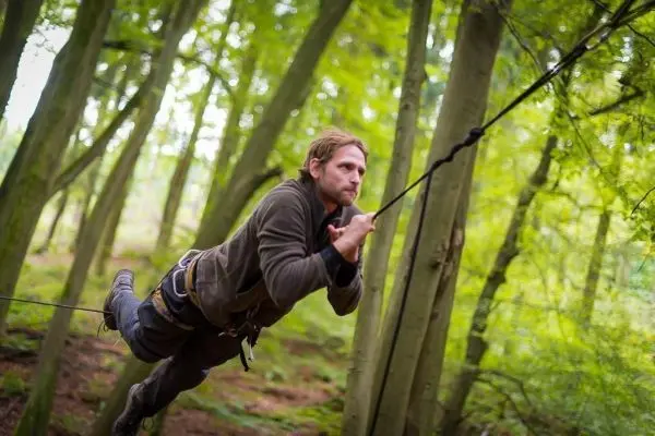 Mann überquert selbstgebaute Seilbrücke zwischen Bäumen im Wald