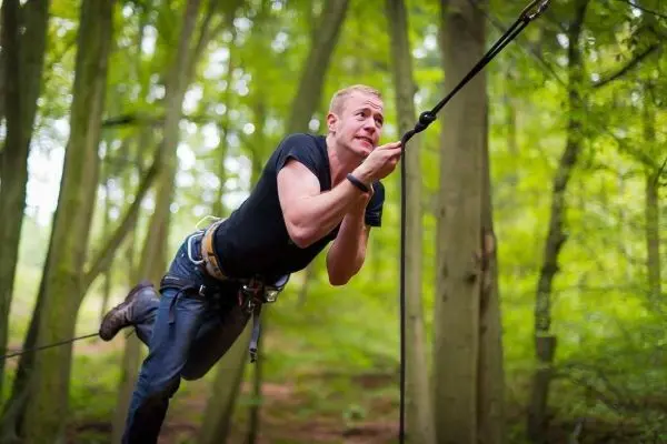 Mann überquert selbstgebaute Seilbrücke zwischen Bäumen im Wald