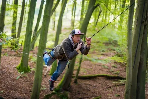 Mann überquert selbstgebaute Seilbrücke zwischen Bäumen im Wald