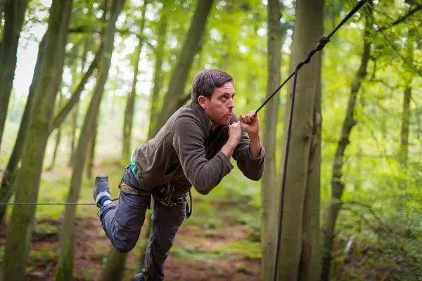 Mann überquert selbstgebaute Seilbrücke zwischen Bäumen im Wald