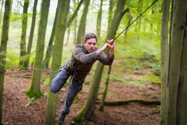 Mann überquert selbstgebaute Seilbrücke zwischen Bäumen im Wald