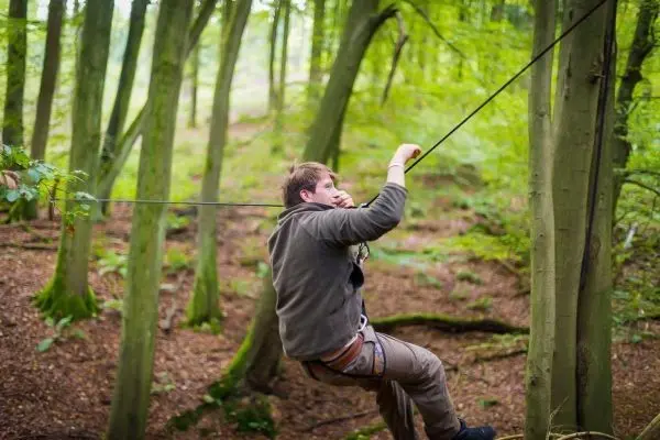 Mann überquert selbstgebaute Seilbrücke zwischen Bäumen im Wald