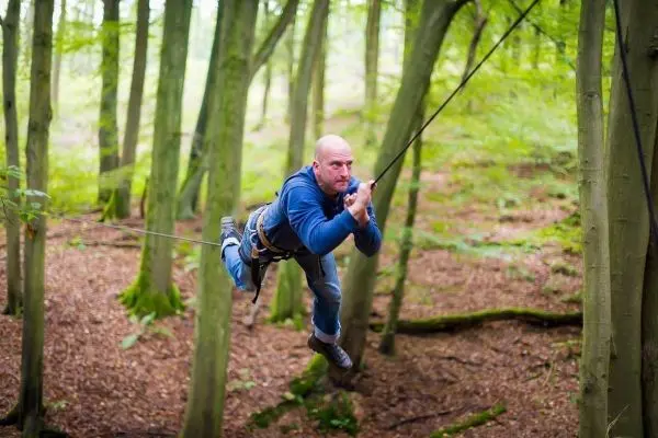 Mann überquert selbstgebaute Seilbrücke zwischen Bäumen im Wald