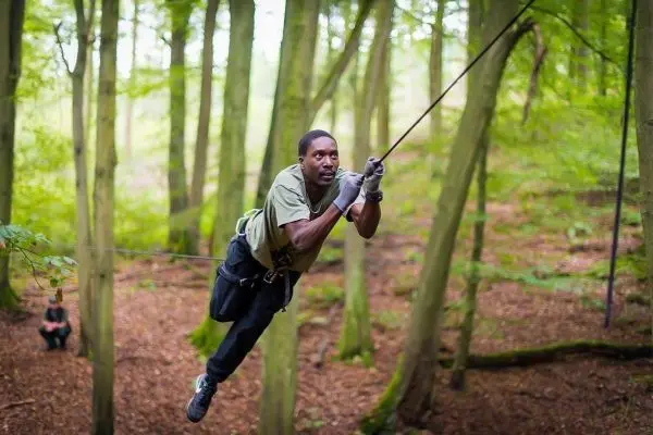 Mann überquert selbstgebaute Seilbrücke zwischen Bäumen im Wald