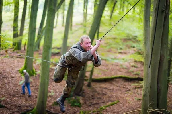 Mann überquert selbstgebaute Seilbrücke zwischen Bäumen im Wald