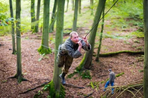 Mann überquert selbstgebaute Seilbrücke zwischen Bäumen im Wald