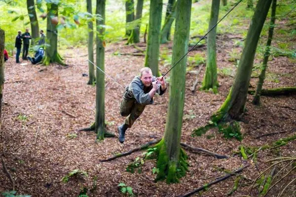 Mann überquert selbstgebaute Seilbrücke zwischen Bäumen im Wald