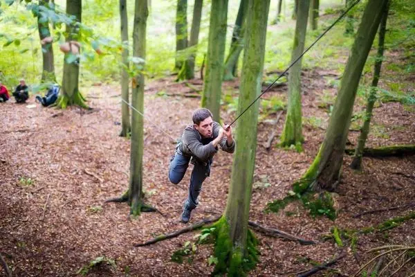 Mann überquert selbstgebaute Seilbrücke zwischen Bäumen im Wald