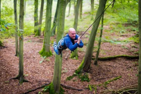 Mann überquert selbstgebaute Seilbrücke zwischen Bäumen im Wald
