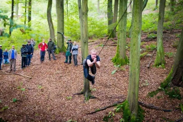Mann überquert selbstgebaute Seilbrücke zwischen Bäumen im Wald