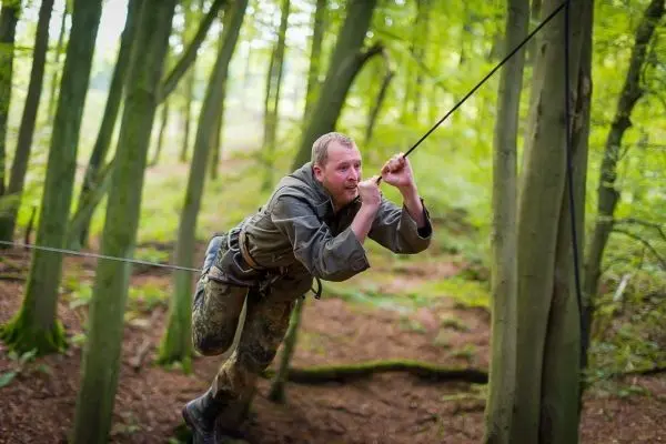 Mann überquert selbstgebaute Seilbrücke zwischen Bäumen im Wald