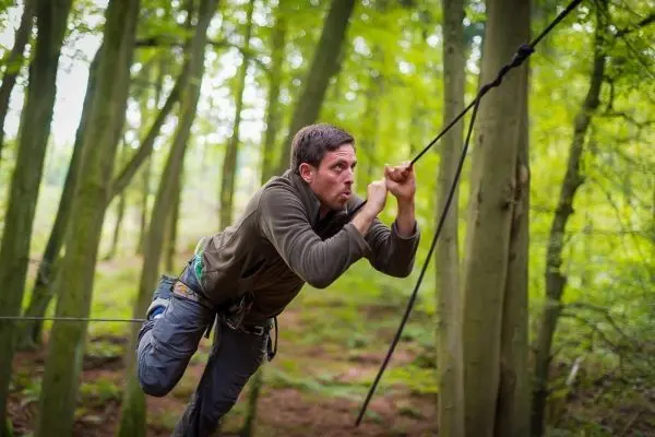 Mann überquert selbstgebaute Seilbrücke zwischen Bäumen im Wald
